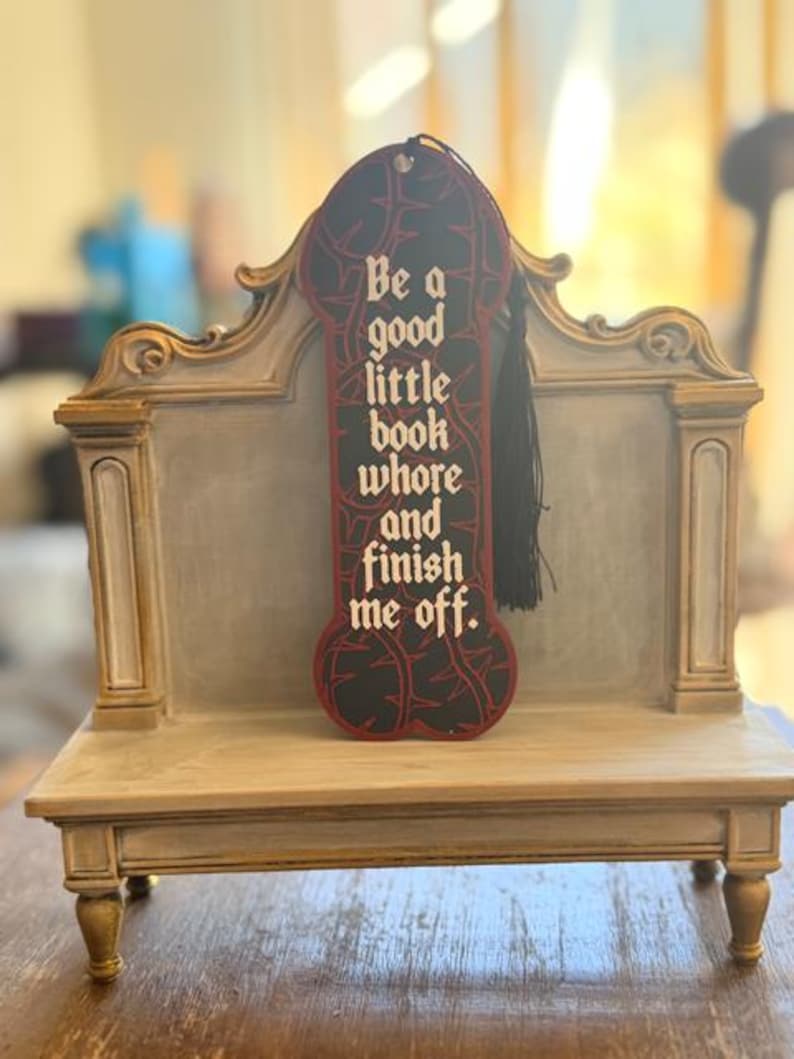 Black thorn vine bookmark with white gothic lettering and black tassel displayed on a purple and gold bench