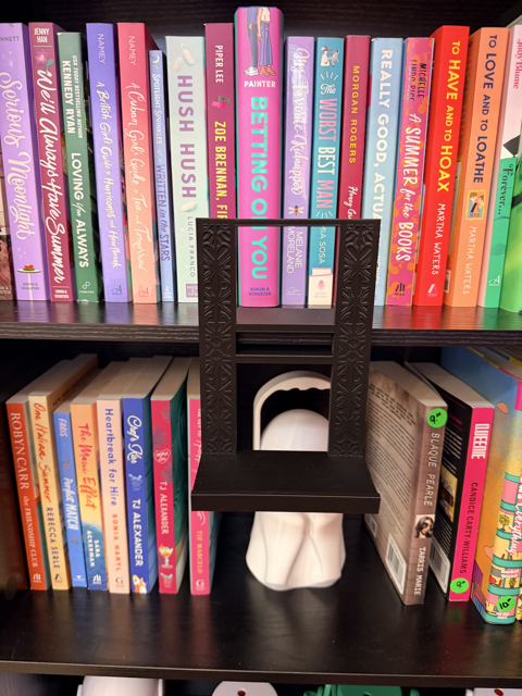 Straight-on view of the black Floating Bookshelf Ledge clipped over a shelf in front of colorful books