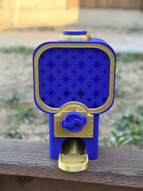 Blue and gold fantastic vending machine 3D printed by Gossamer Creations, with a star patterned window, blue swirl dial, and gold catch tray