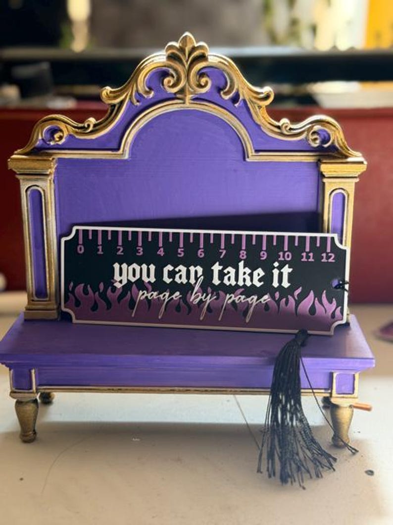 Ruler bookmark with flame design and black tassel displayed on a purple and gold bench